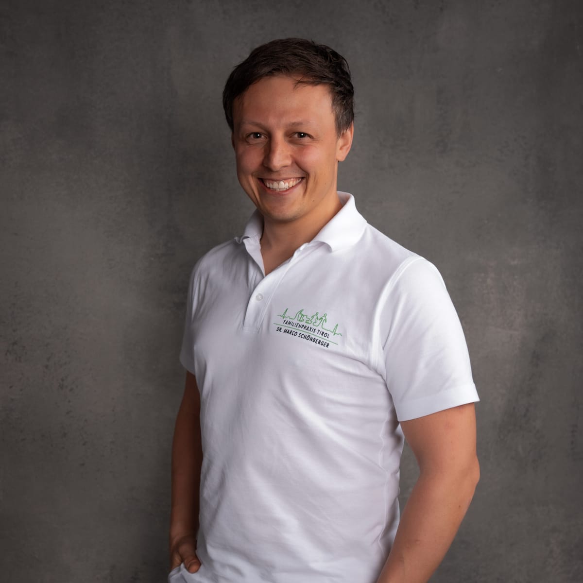 Dr Marco Schönberger, travel medicine doctor in Wörgl, wearing a white coat against a grey background.