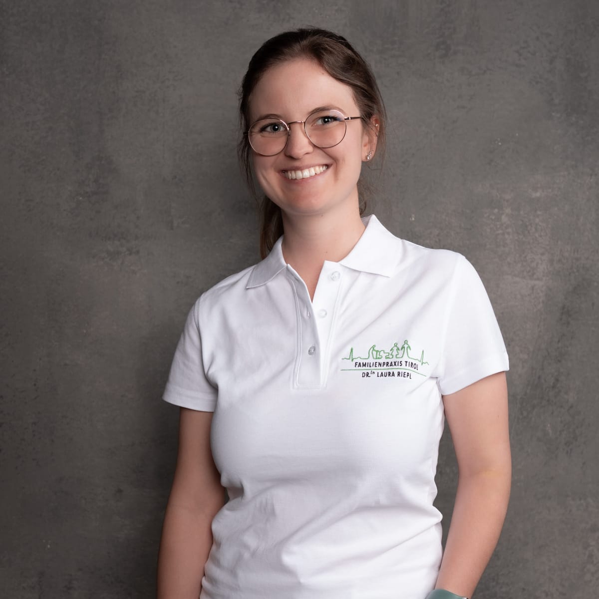 Dr Laura Riepl wearing white professional attire against a grey background.